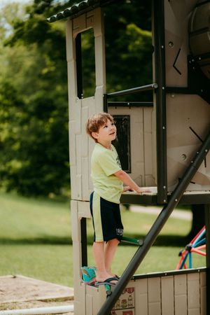 A young child in a yellow t-shirt climbing on a playground structure on a sunny day.
