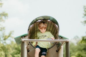 A child plays in a green outdoor playground structure during a sunny day.