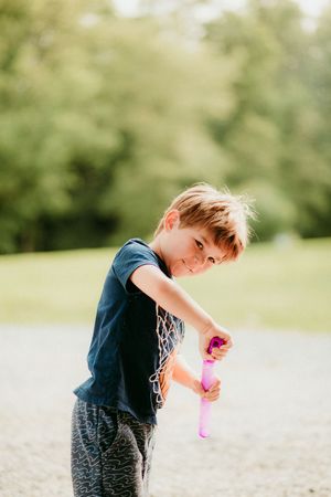 A child plays with pink bubbles outdoors on a sunny day against a blurred green background.