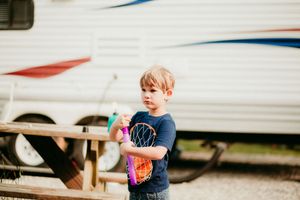 A child wearing a navy t-shirt stands near a trailer while holding a colorful drink on a sunny day.