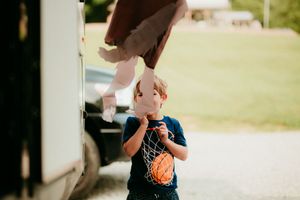 A young boy in a navy blue t-shirt stands holding an ice cream cone outdoors on a sunny day.