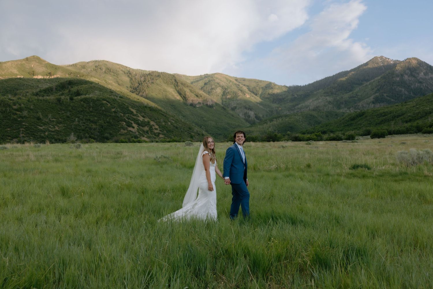 Couple in formal attire stands on red rock overlook with dramatic canyon vista of Zion National Park in background.