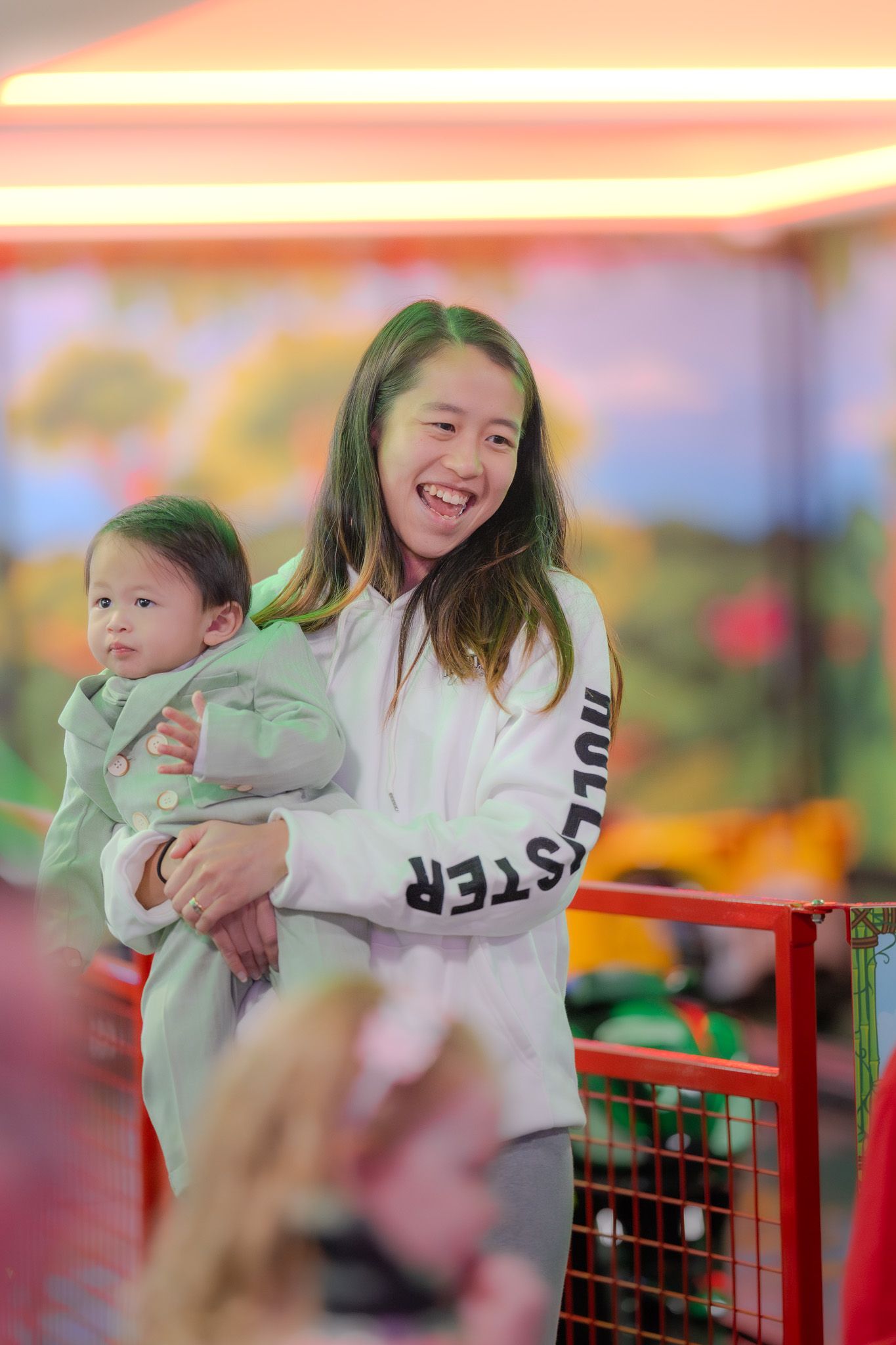 A cheerful moment at an amusement park with someone wearing a white jacket holding a young child in casual attire.