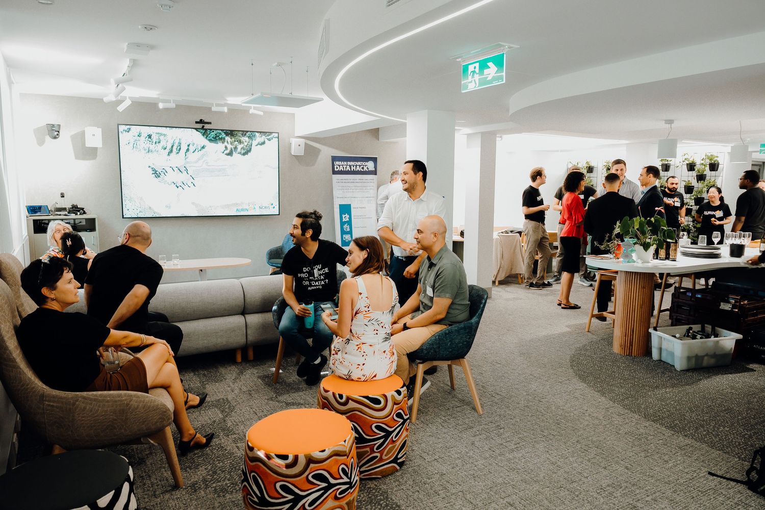 People gather in a modern office space with grey carpet and curved walls for a casual business meeting.