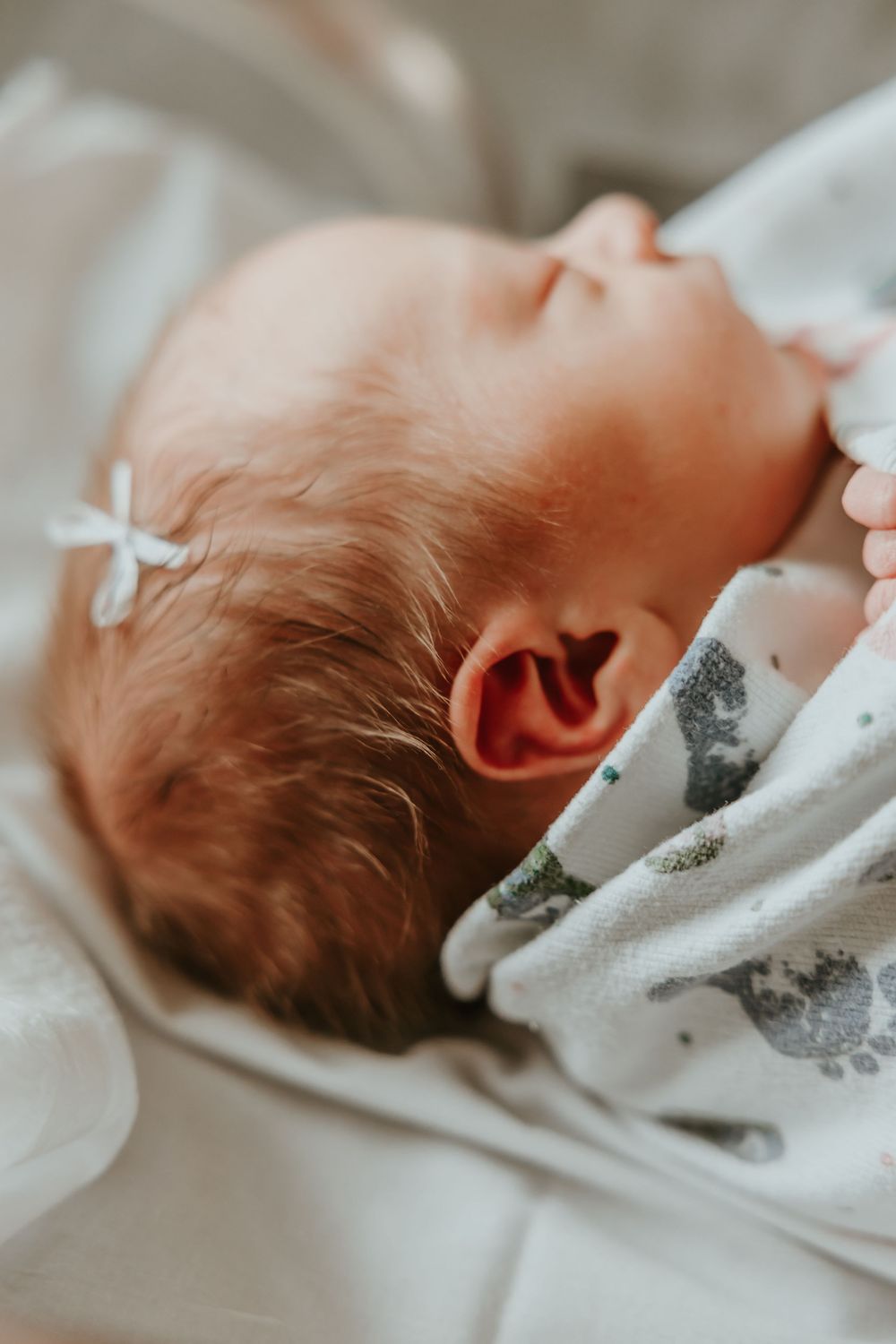 Close-up view of a sleeping baby's head resting on soft white and grey patterned bedding.