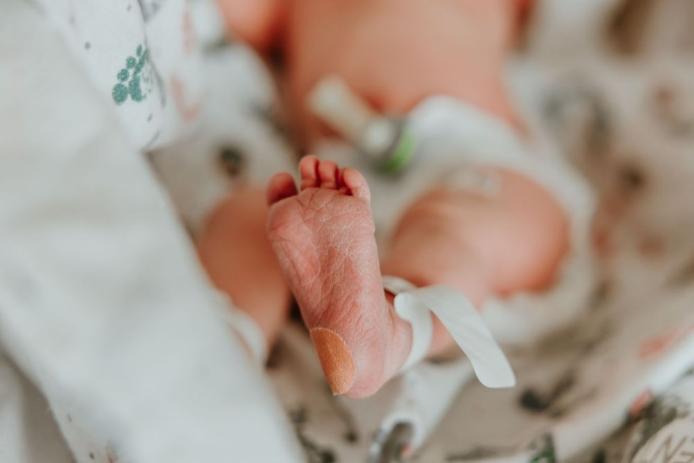 Tiny newborn baby foot with delicate toes resting on white and floral patterned fabric.