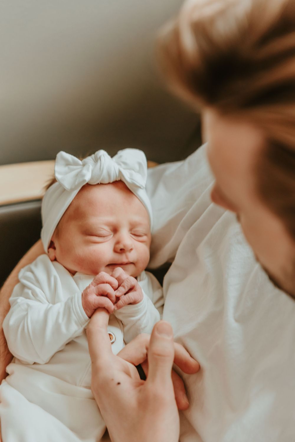 Newborn baby in white outfit with bow sleeping peacefully.
