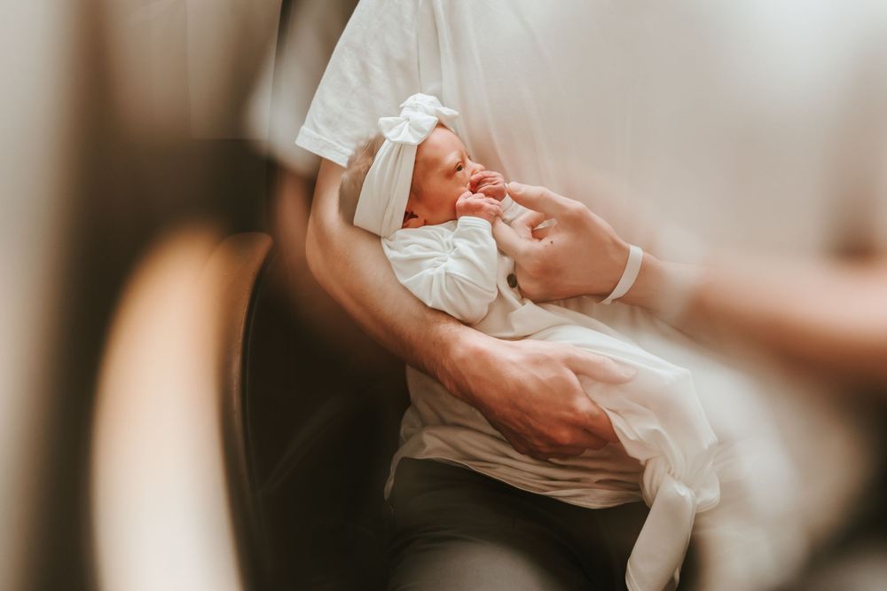 A tender moment as a newborn baby is cradled gently in white fabric.