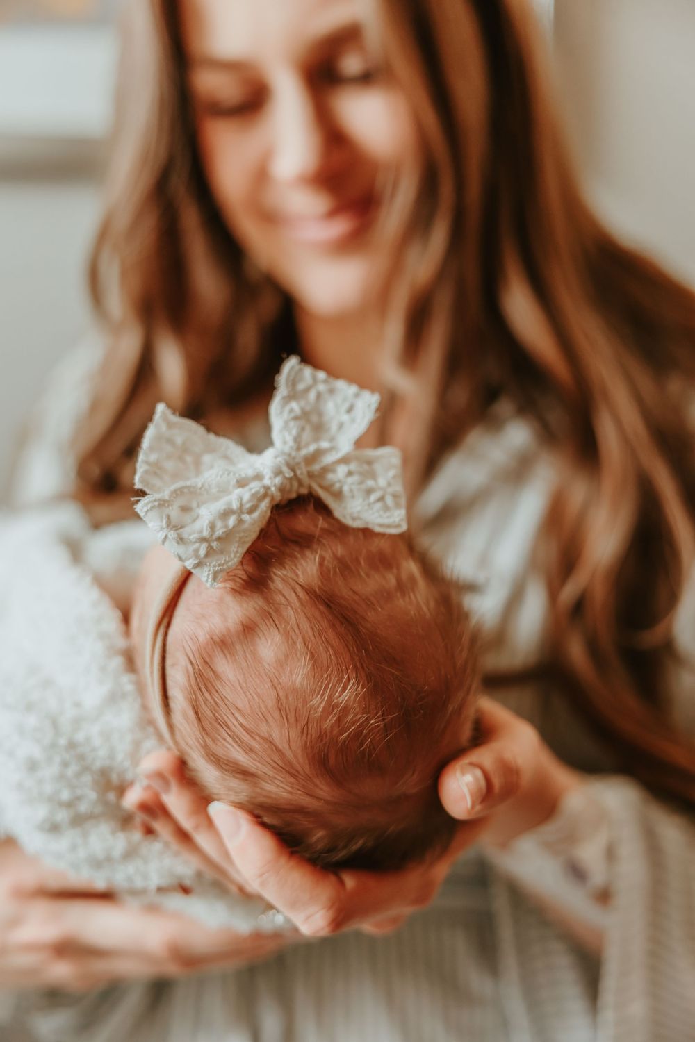 Gentle hands cradle a sleeping newborn wearing a delicate lace headband.