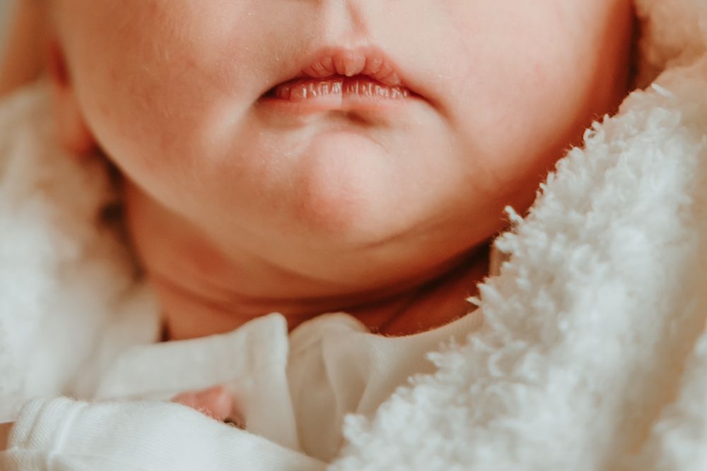 A soft close-up macro photo of an infant snuggled in a white blanket showing their chin and lips.