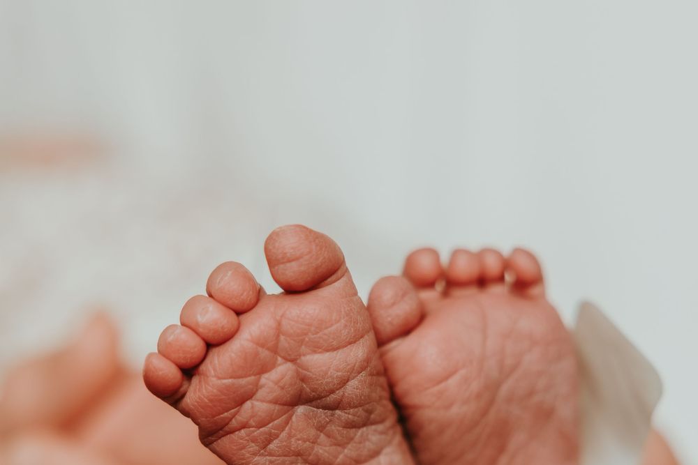 Close-up view of tiny newborn baby feet with wrinkled skin against a light background.