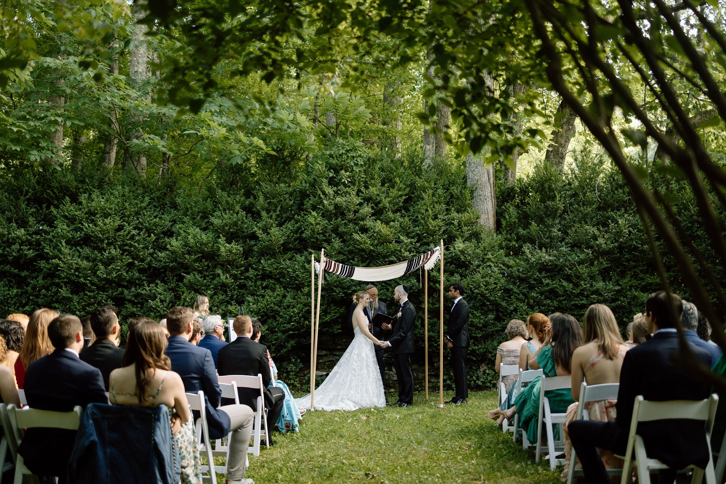 Outdoor wedding ceremony in a lush green garden with white chairs and a fabric canopy altar arrangement.