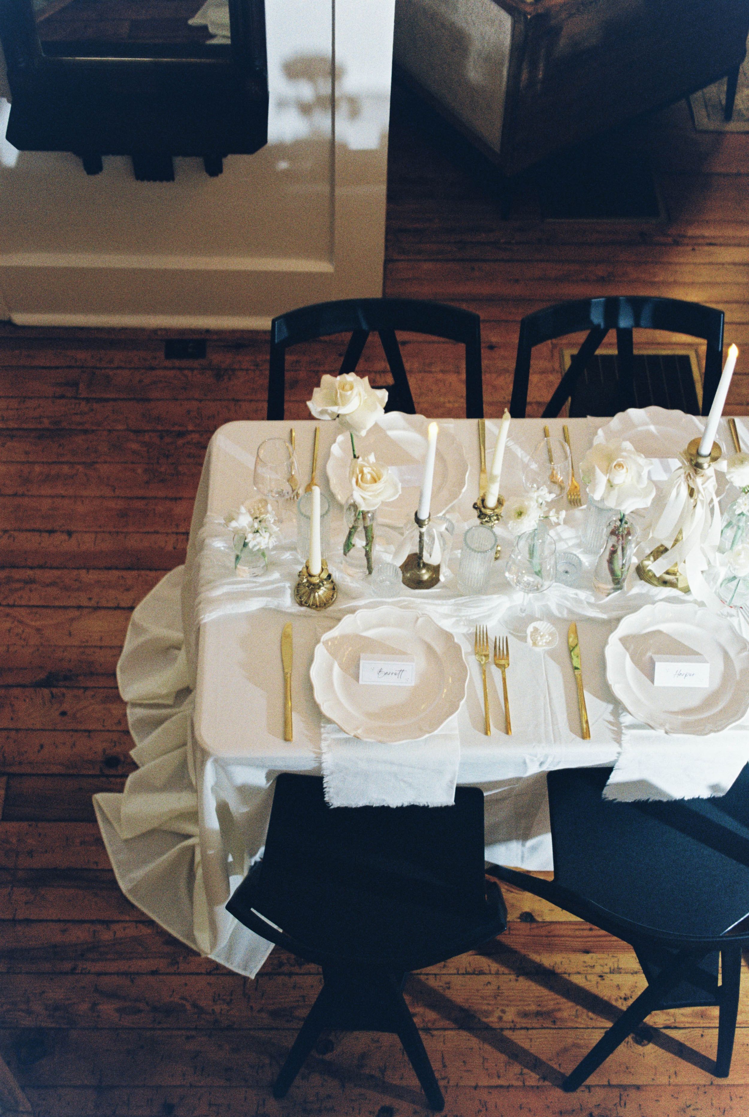 An elegant table setting with white linens, gold cutlery, and delicate floral centerpieces arranged on a wooden floor.