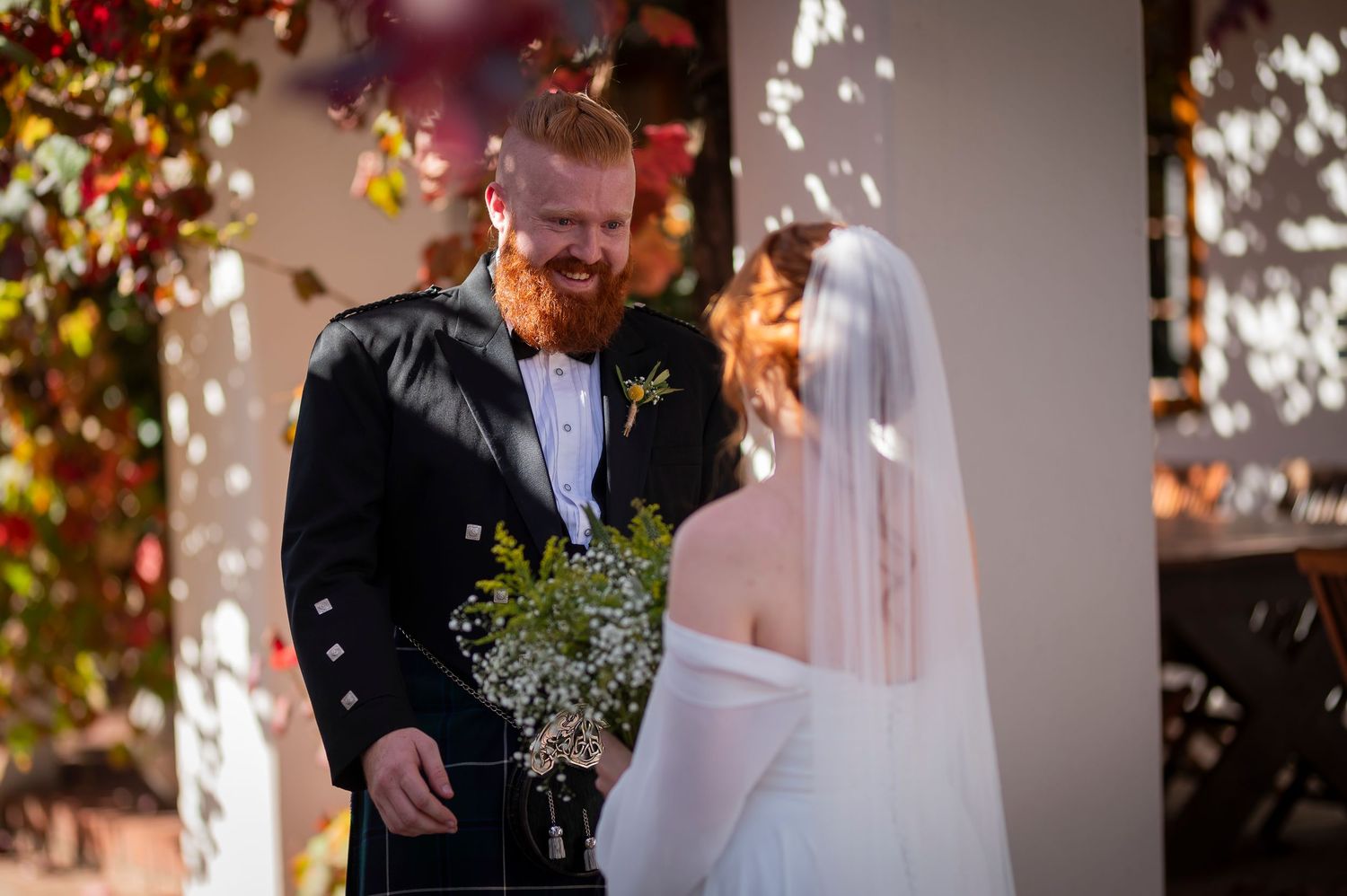 Romantic wedding moment captured under twinkling lights and autumn foliage.