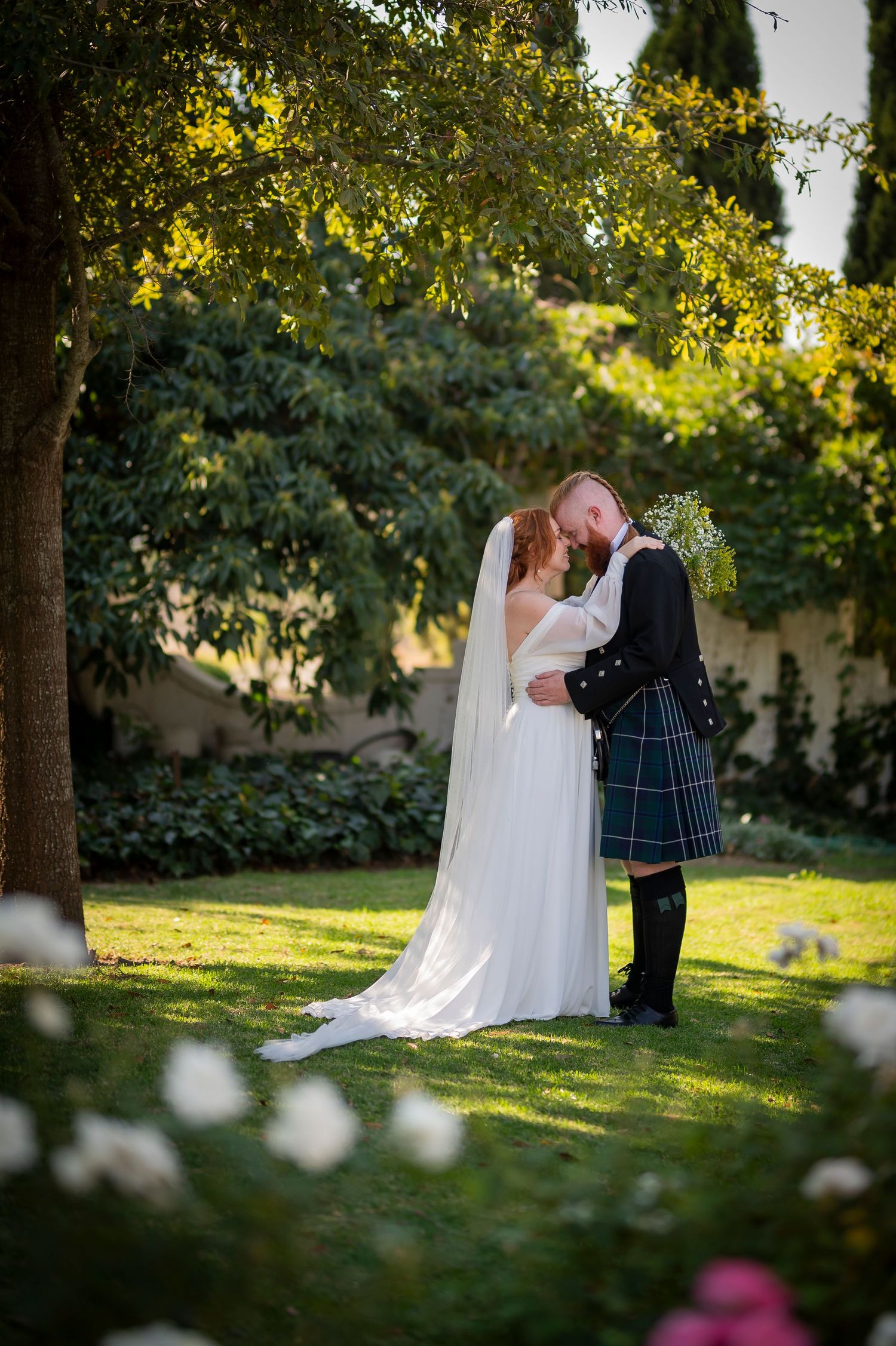 Newlyweds share romantic moments in a sunlit garden setting.