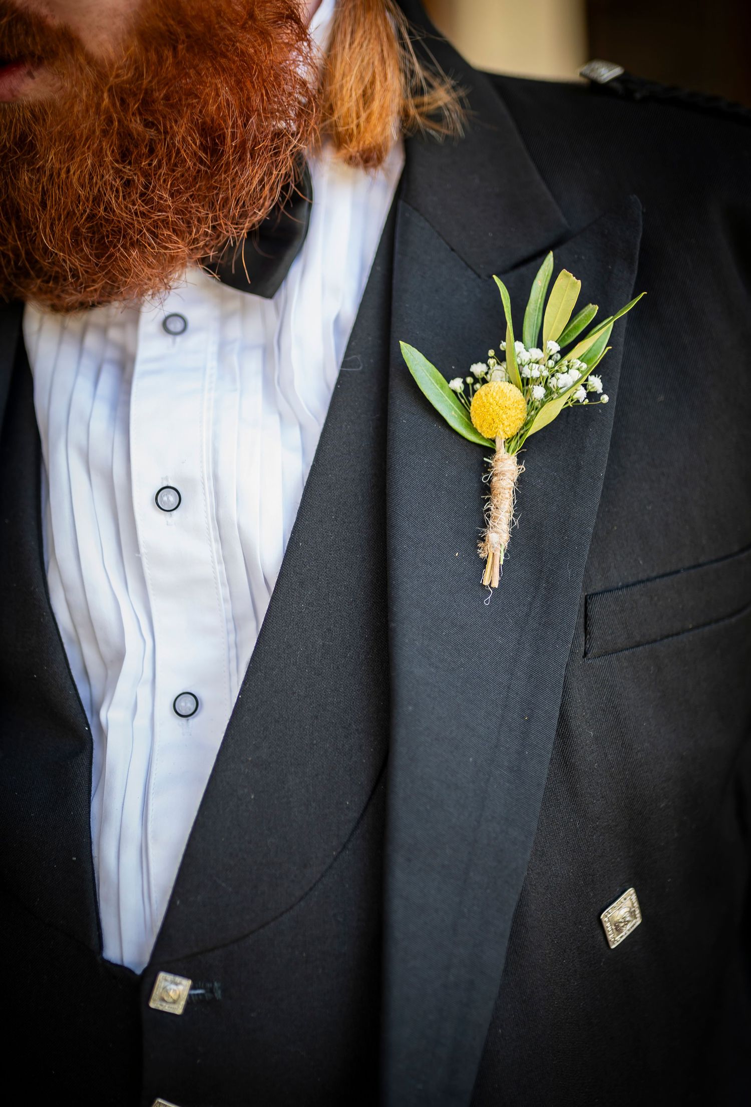 Row of groomsmen's boutonnieres featuring yellow flowers and natural twine wraps on dark suits.