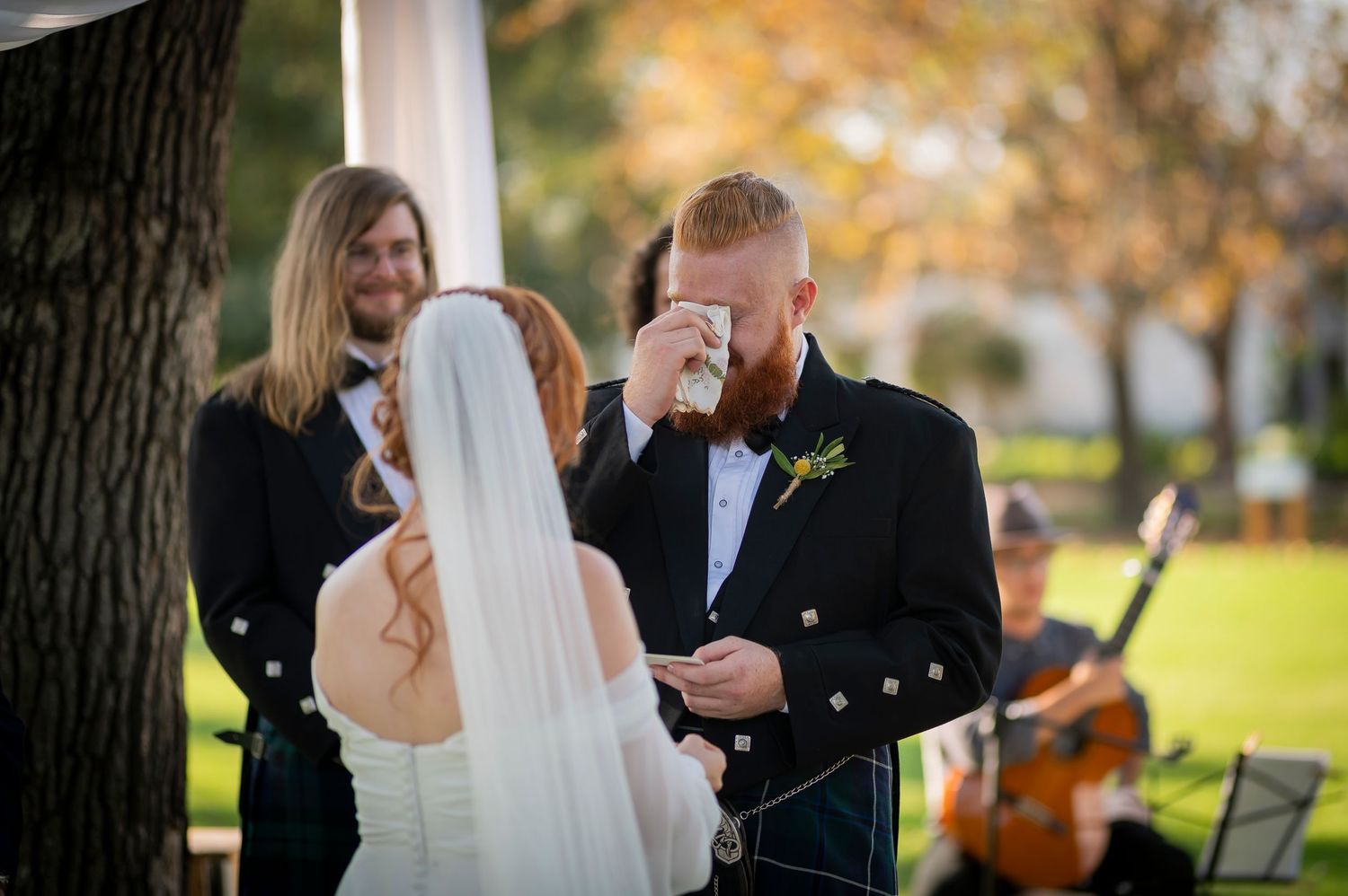 Traditional Scottish wedding ceremony takes place outdoors with bride in white dress and groom in formal kilt attire.