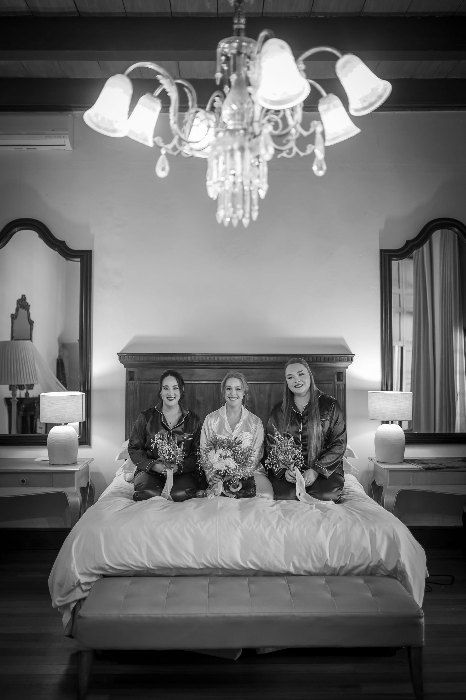 Friends lounging on large bed in formal attire during wedding preparations.