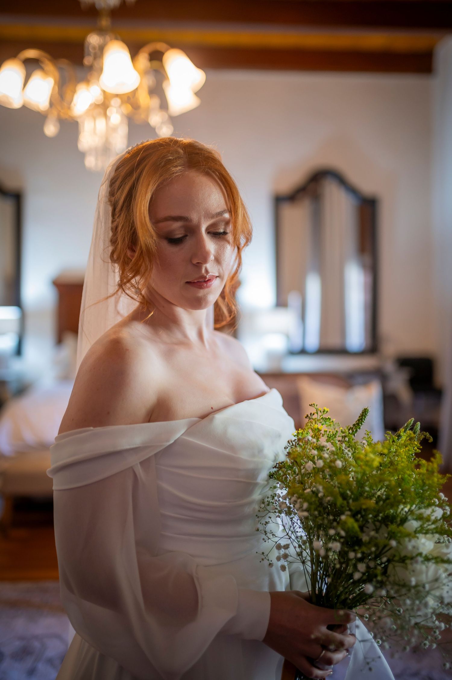 Person in white off-shoulder dress holding delicate green floral arrangement.