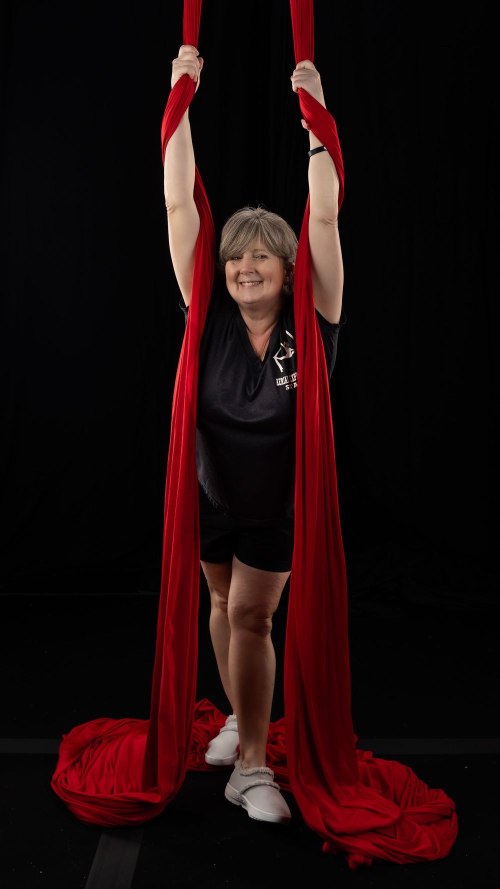 Athletic performer gracefully practices aerial silk moves on vibrant red fabric against black backdrop.