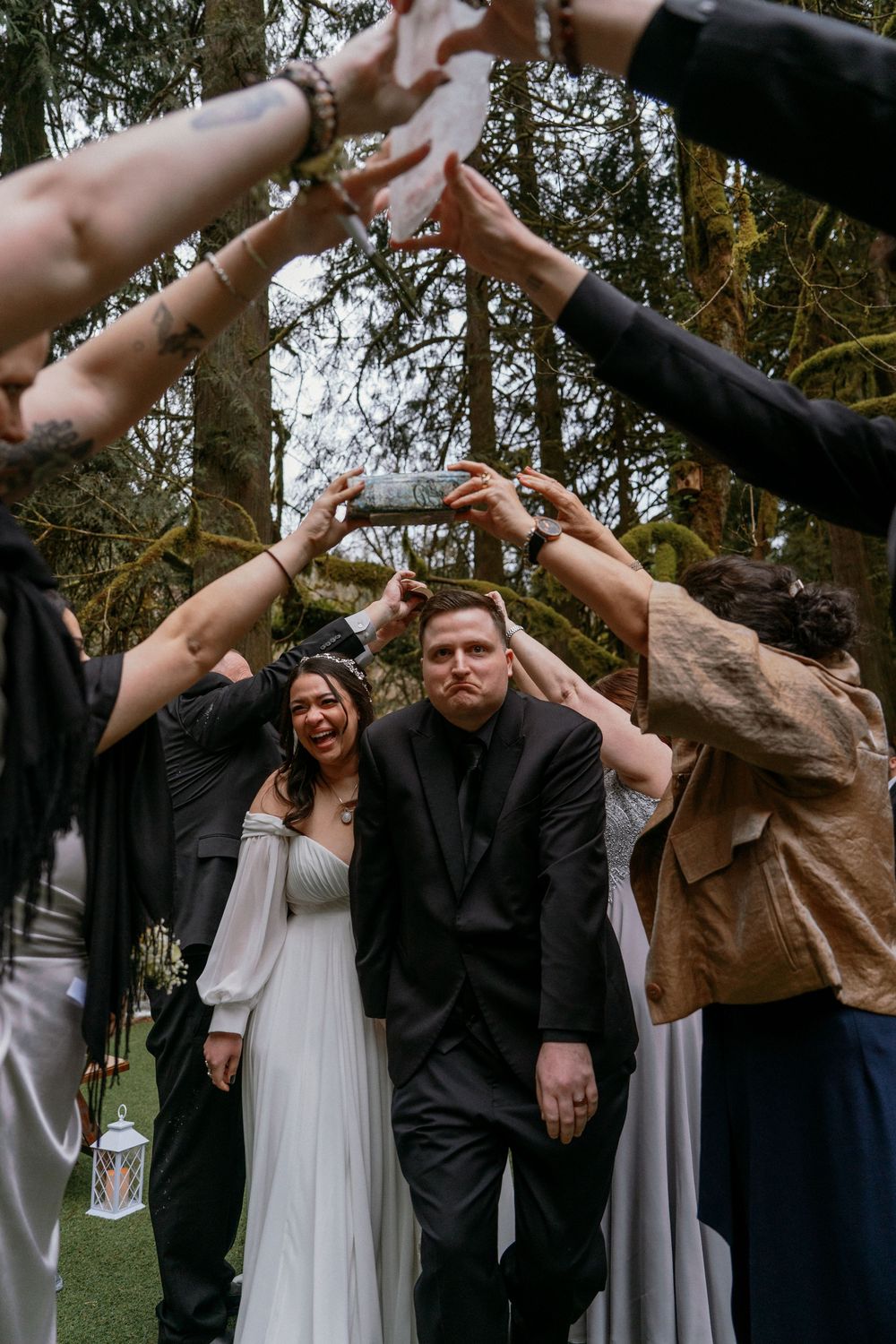 Wedding party creates a tunnel with raised arms as they celebrate in the forest.