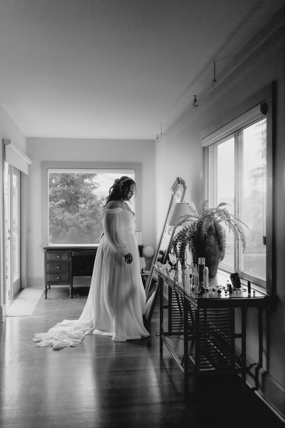 black and white photograph showing elegant wedding dress preparations in a minimalist interior space.