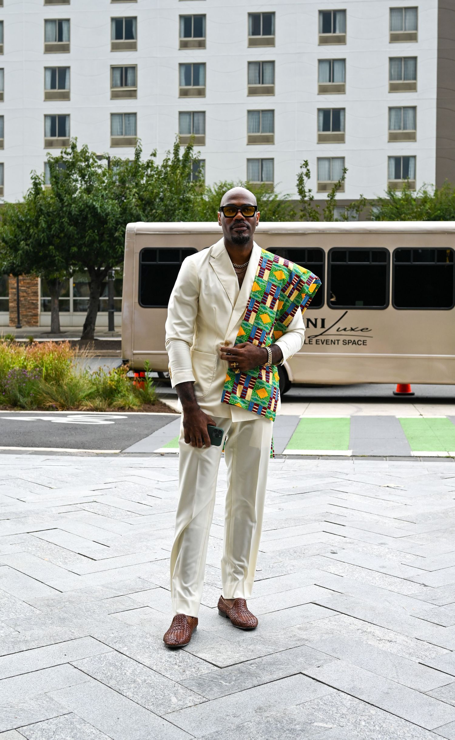 A sequence of someone walking in a white outfit while carrying a colorful patterned bag across a stone plaza.