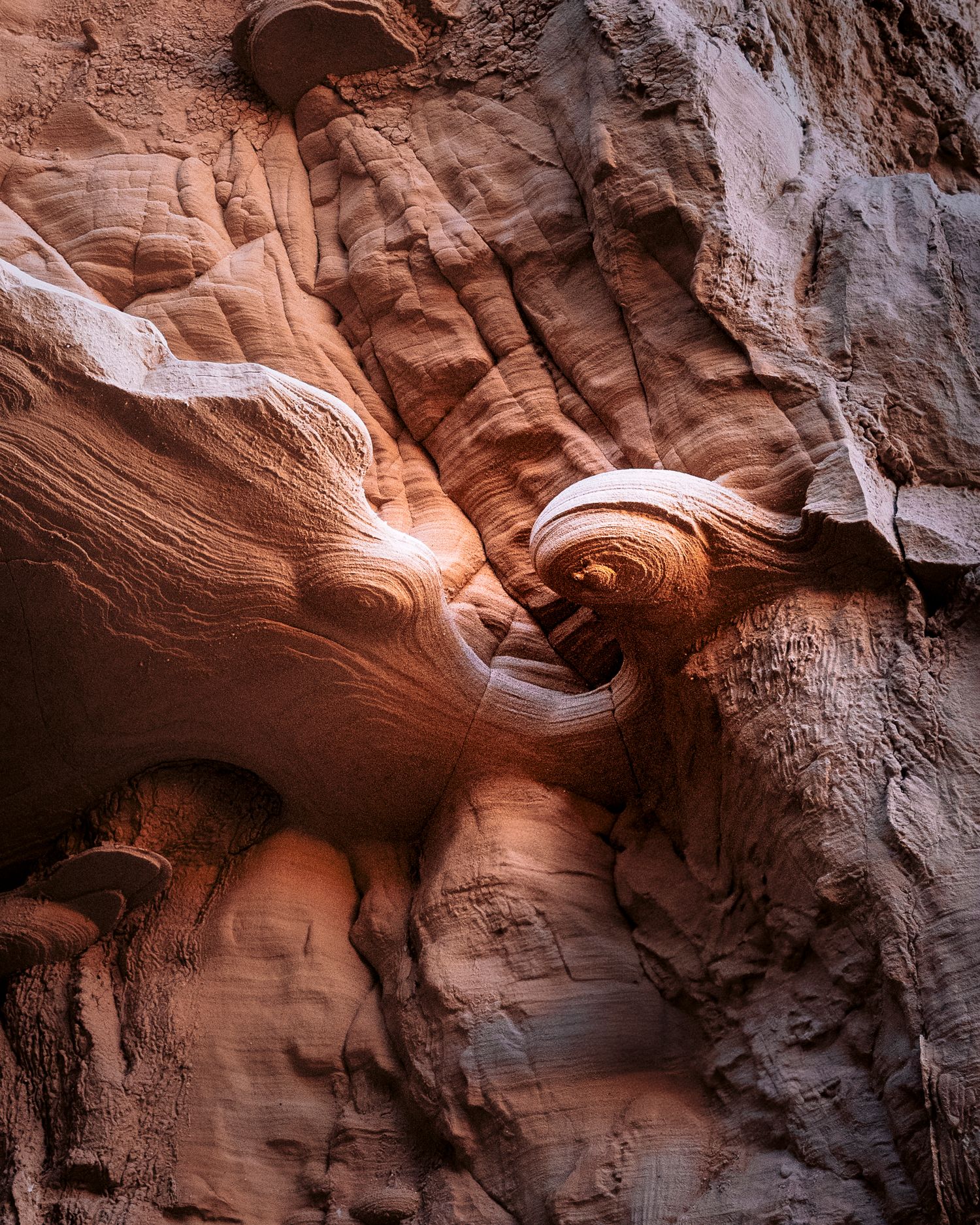 Swirling red sandstone formations inside a narrow slot canyon with warm glowing light.