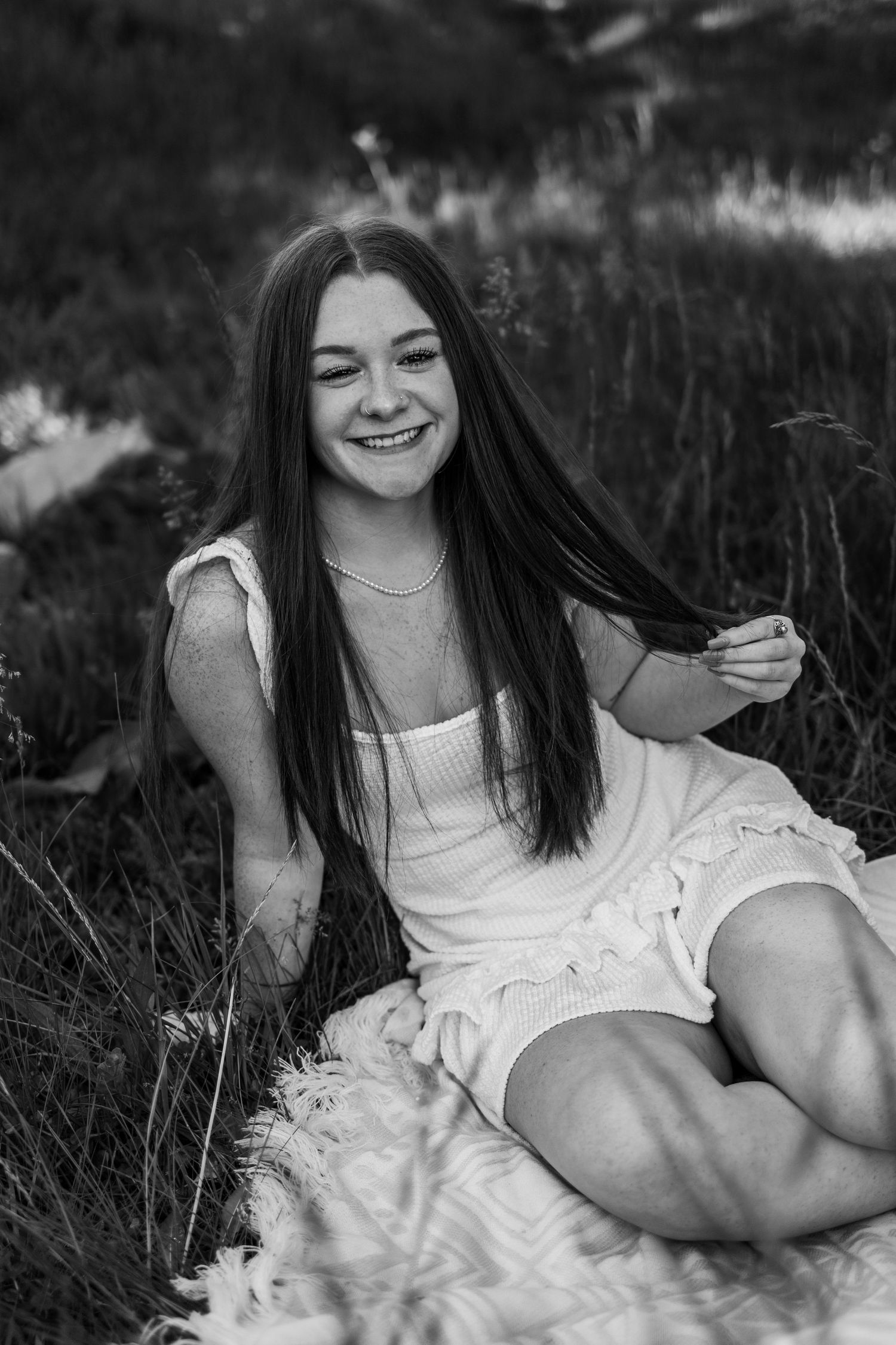 Black and white portrait of a smiling teenage girl with long dark hair sitting in a grassy field.