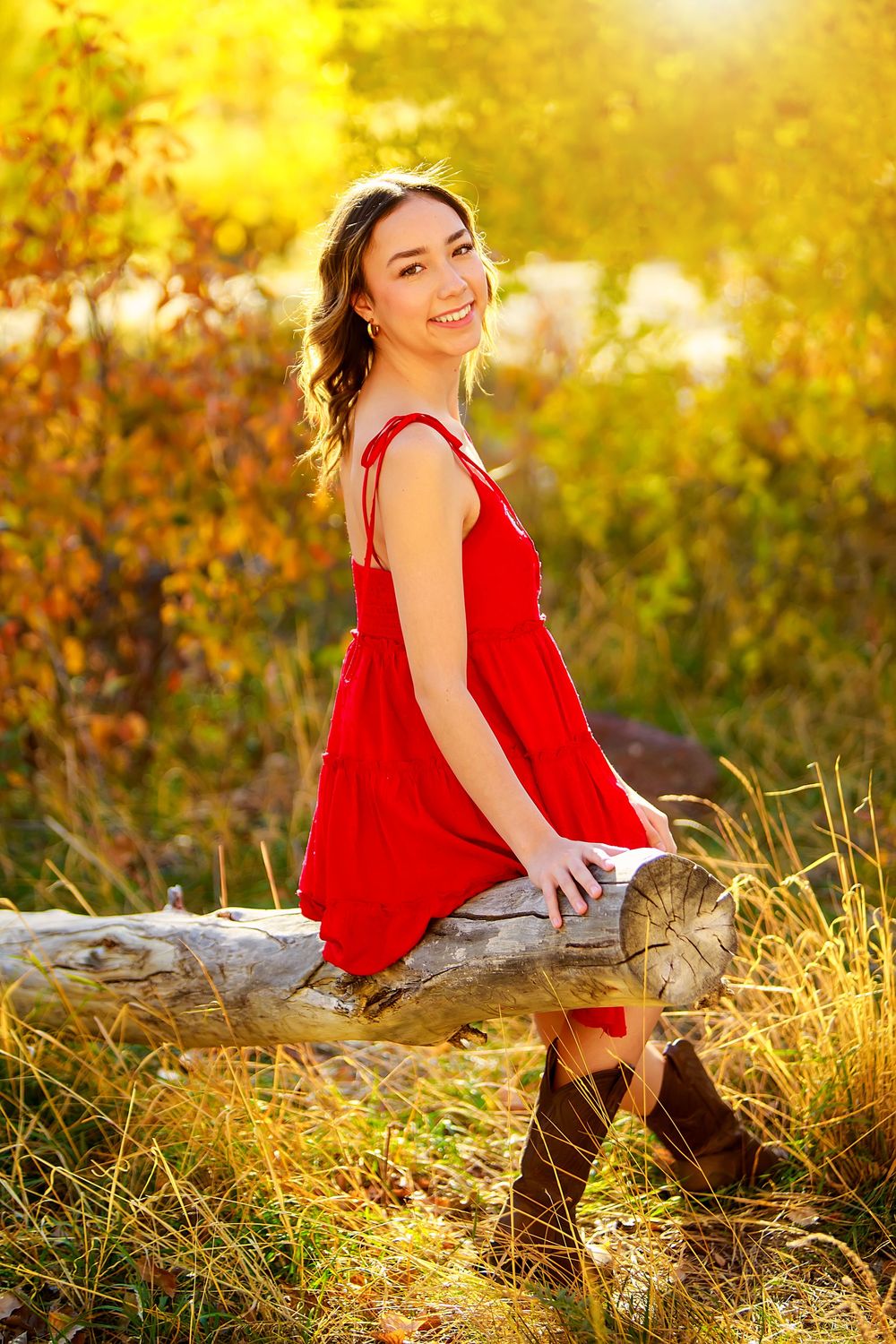 Portrait of someone in red dress sitting on log during golden sunset.