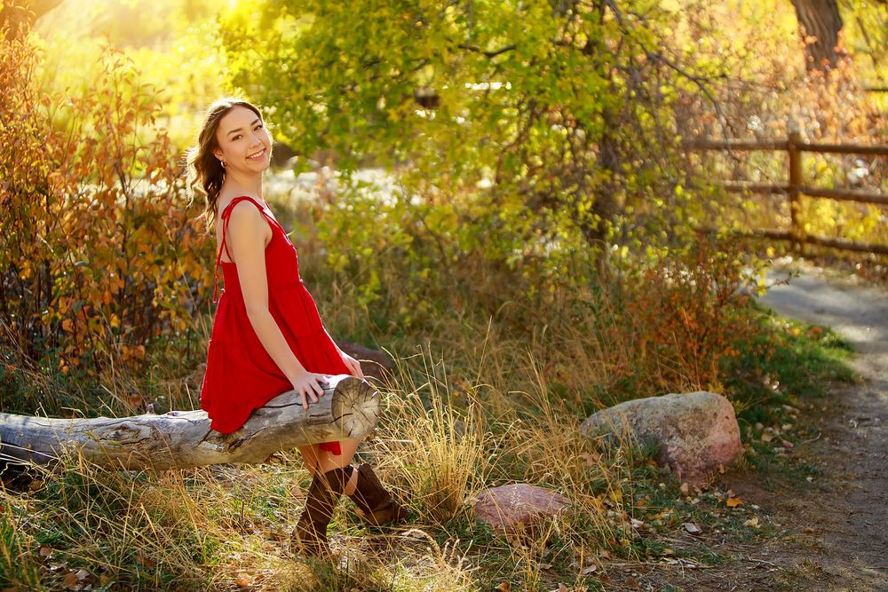 Person in red dress sitting on rock by autumn path with golden light filtering through trees.