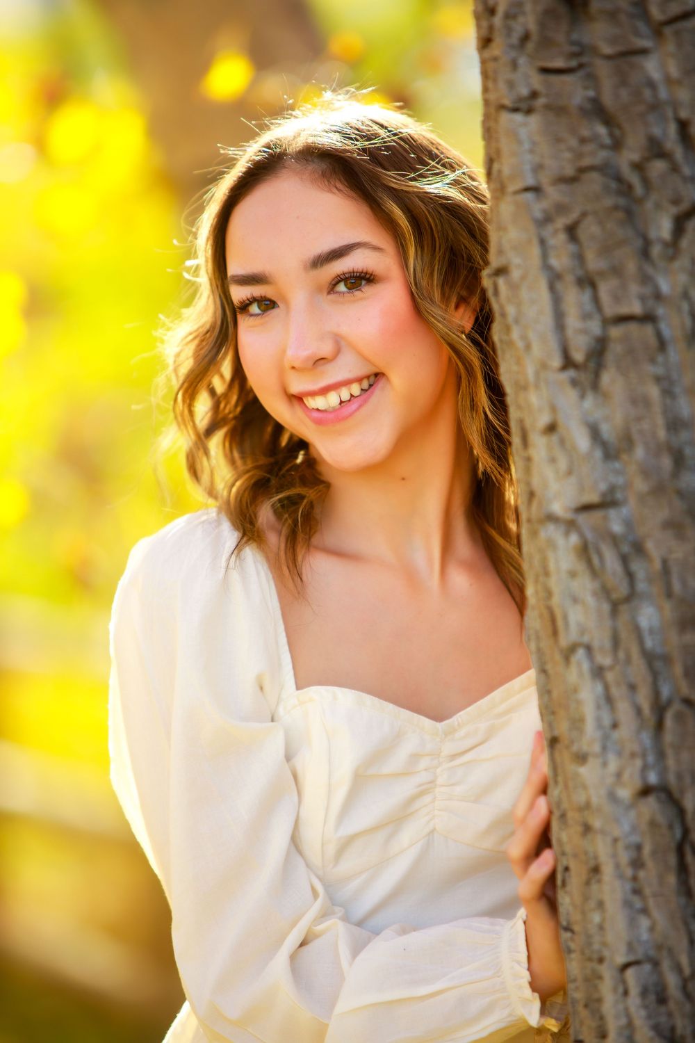 Portrait by tree trunk with autumn colors and soft natural lighting.