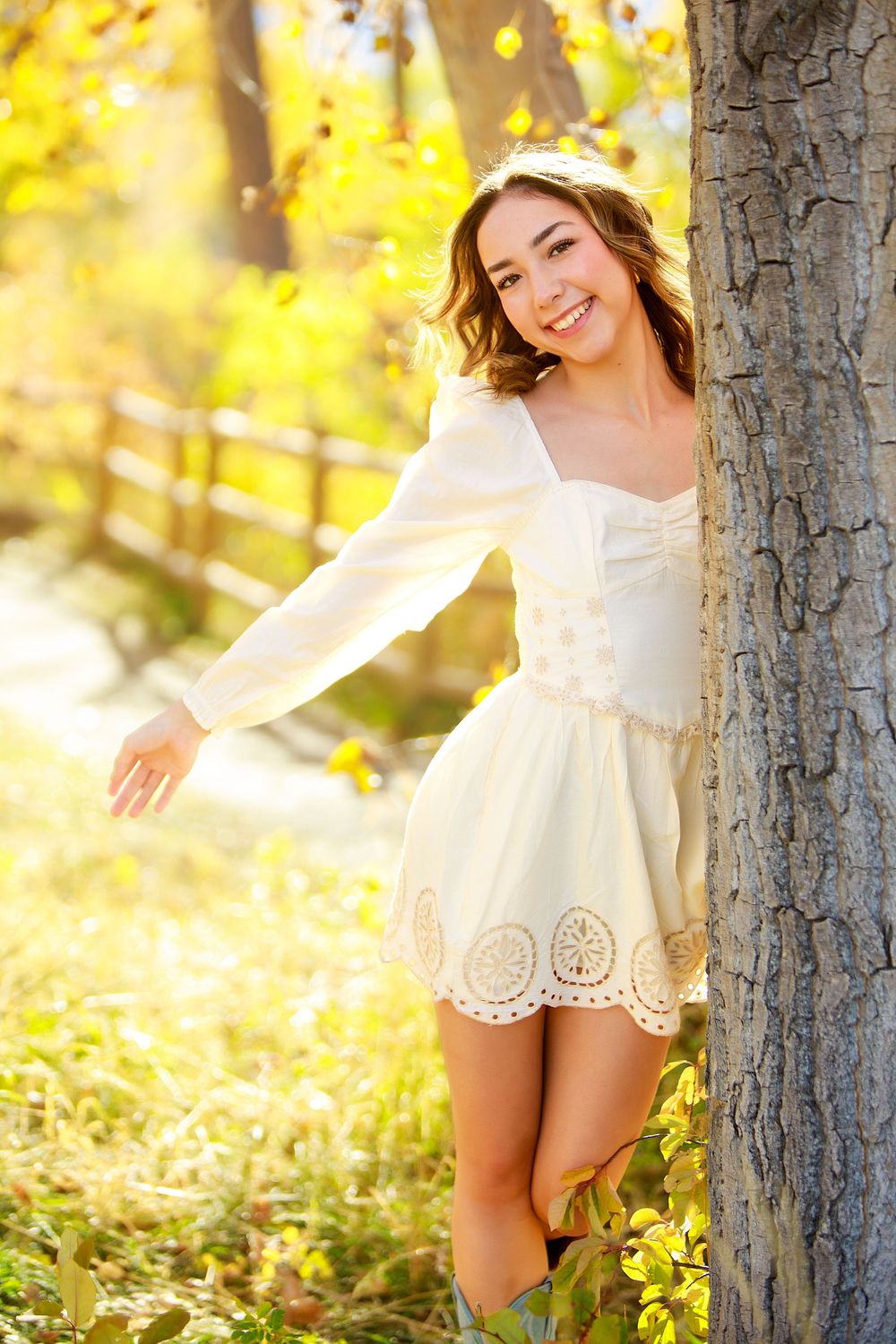 White lace dress portrait against golden autumn scenery and tree trunk.