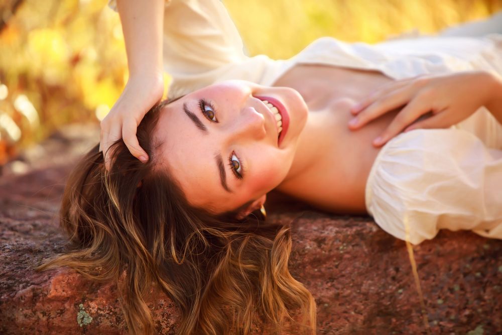 Portrait in white dress lying on rock with golden autumn background and flowing hair.