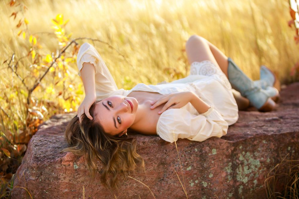 Portrait in white dress lying on rock with golden sunset lighting.