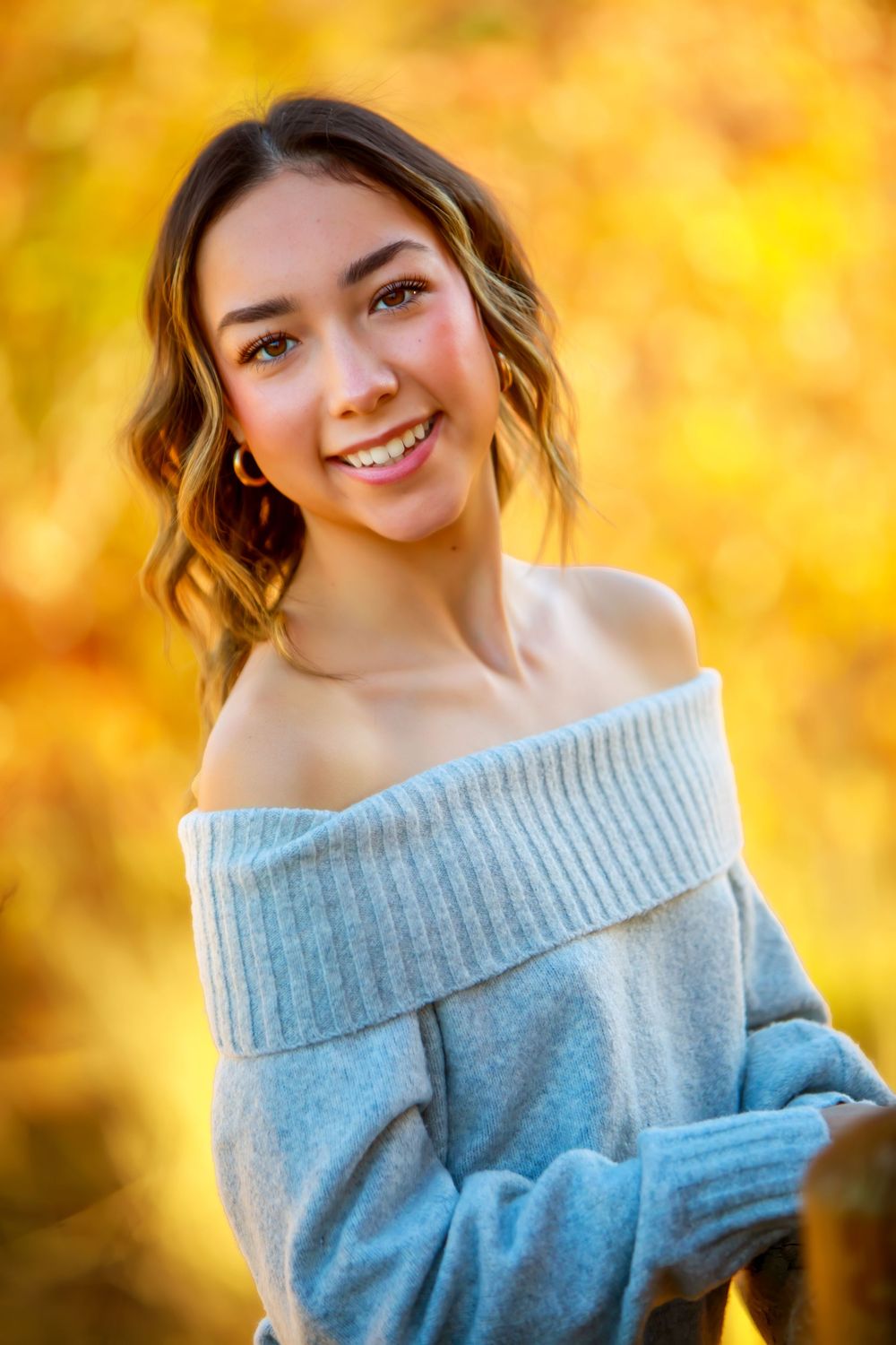 Portrait in cozy gray sweater against warm autumn foliage backdrop.
