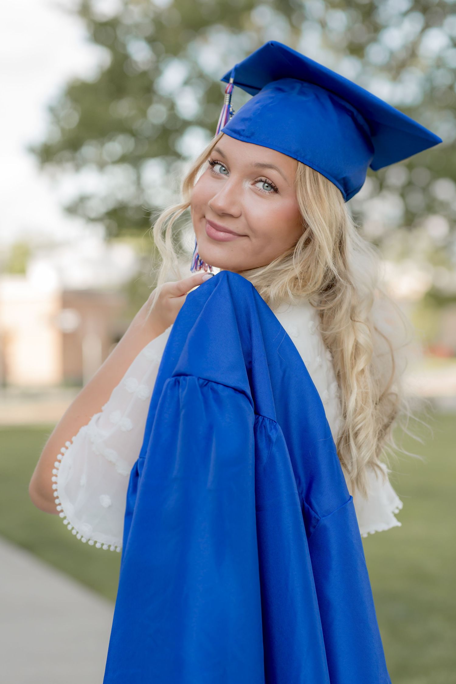 Smiling blonde graduate in blue cap and gown posing outdoors.