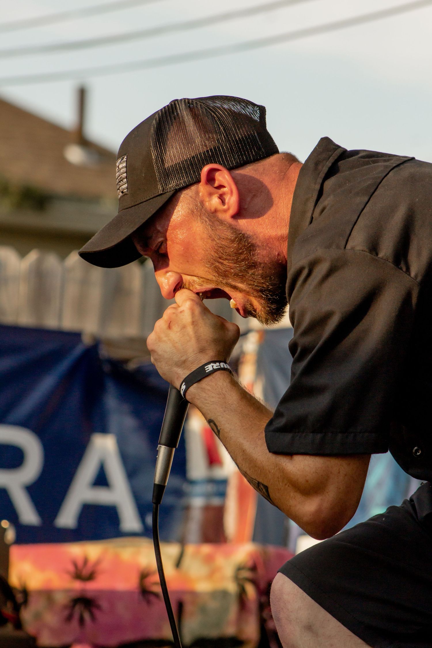 Male singer leaning into microphone with intensity while performing outdoors at a summer event.