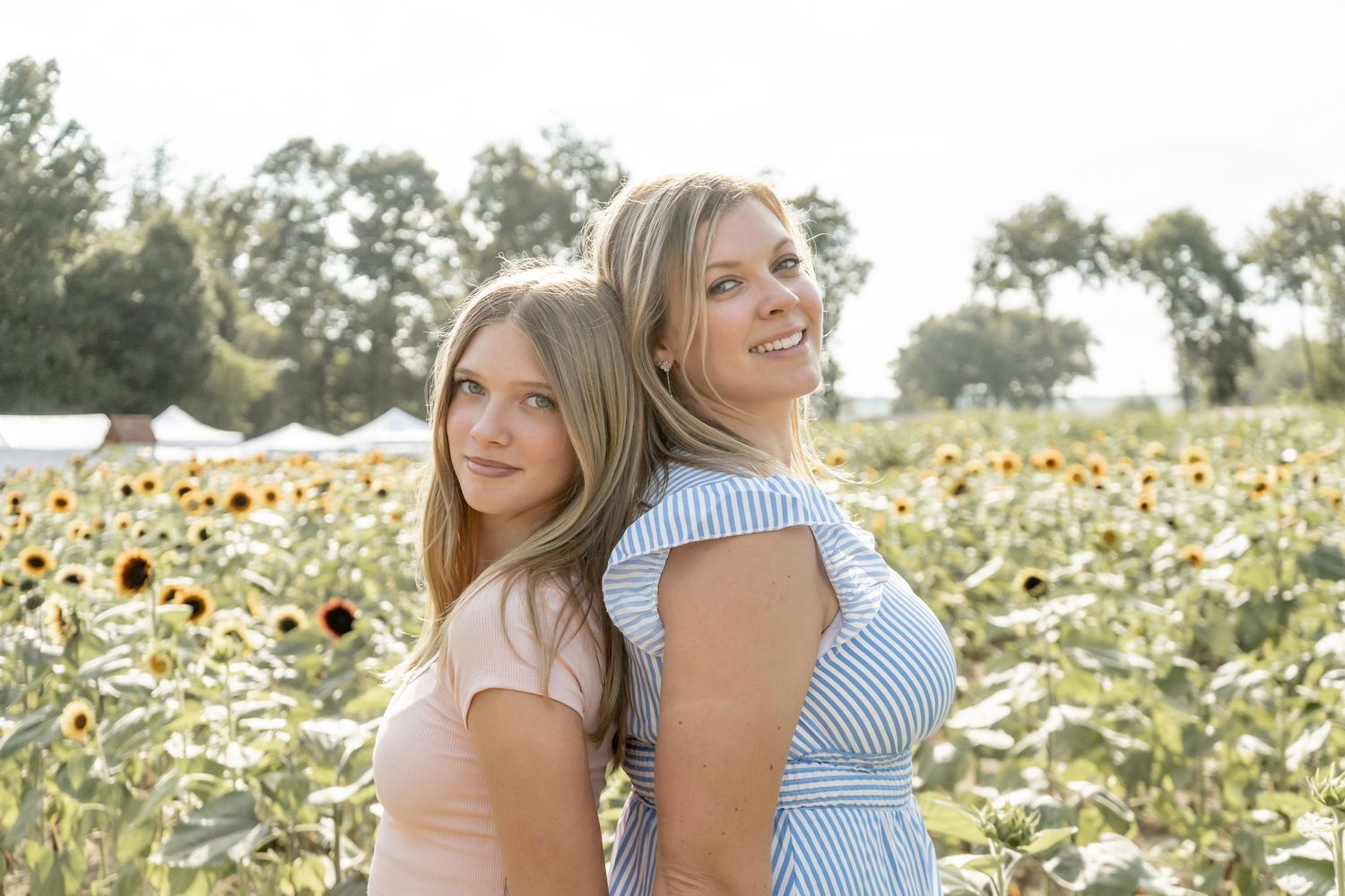 Two women standing back-to-back smiling in a sunflower field.