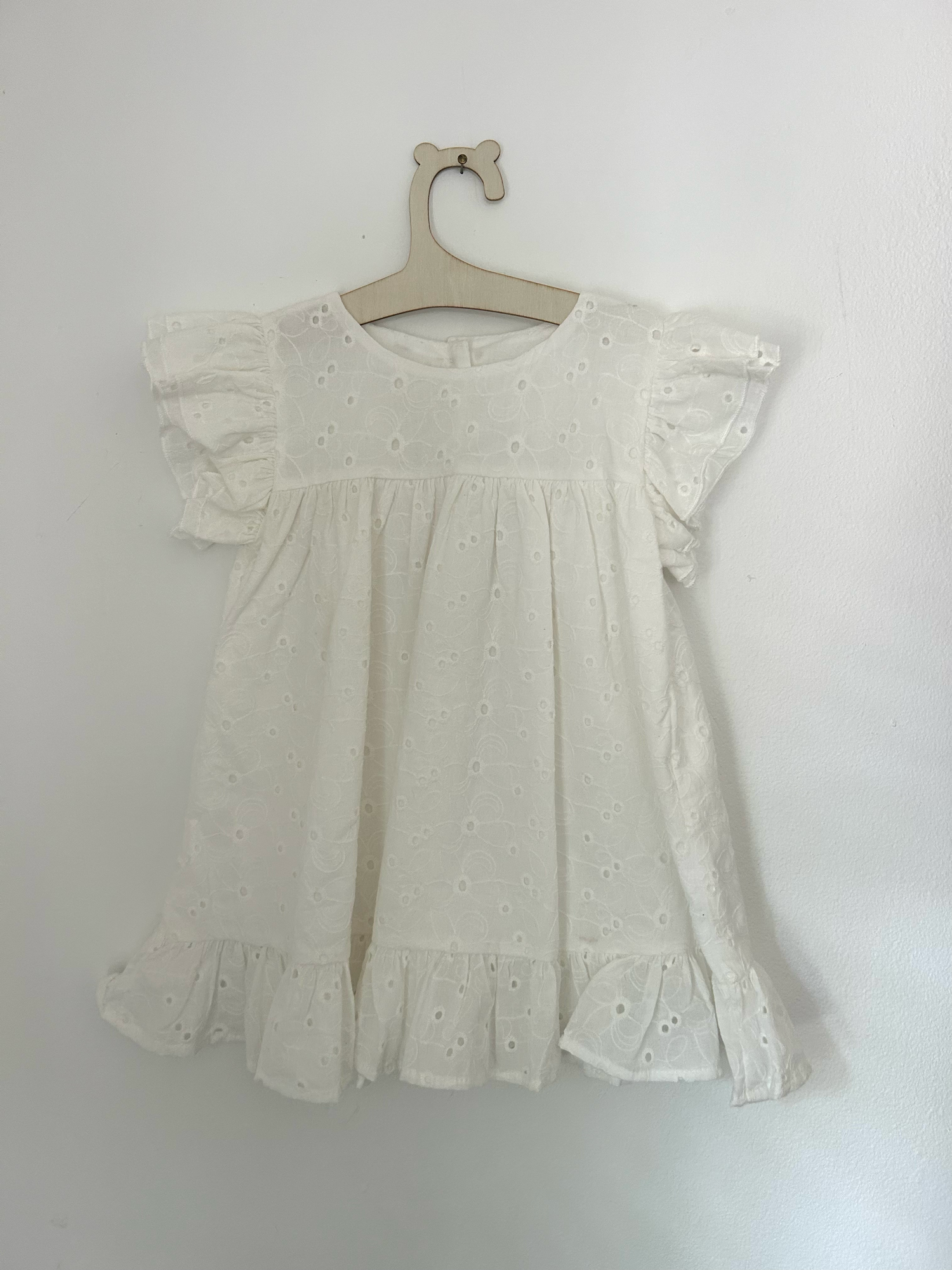 Vintage-style beige knitted baby romper with button details and side pockets hanging on display.