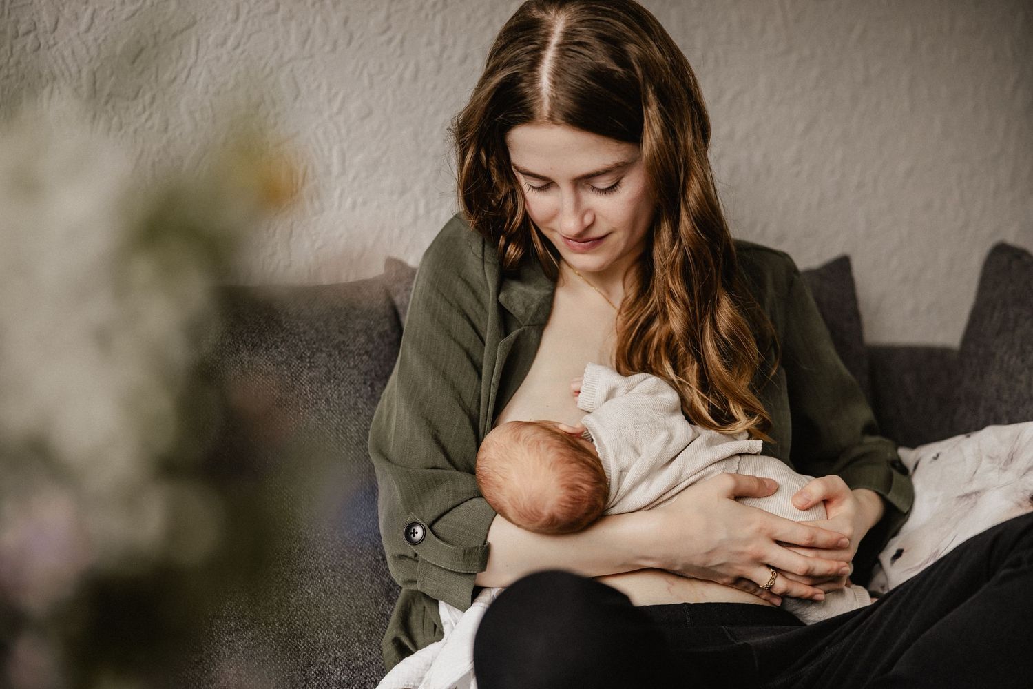 Ein zärtlicher Moment mit Mutter und neugeborenem Baby auf einer grauen Couch stillt. Fotograf wiesbaden