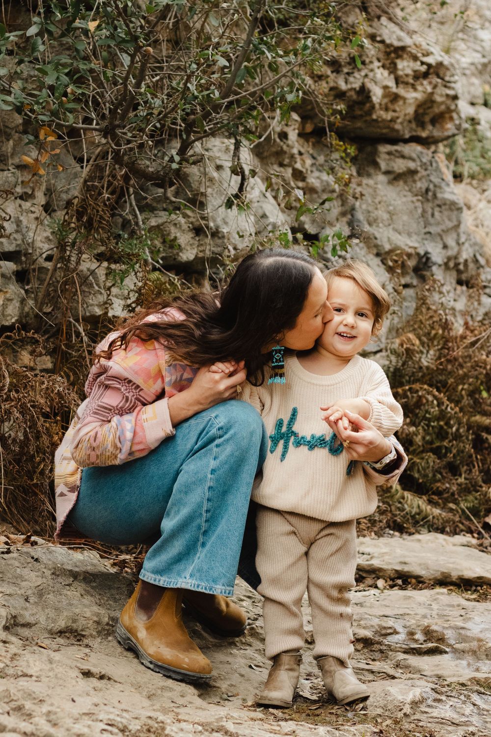 A sweet outdoor moment between two people in casual attire surrounded by natural rock formations and foliage.