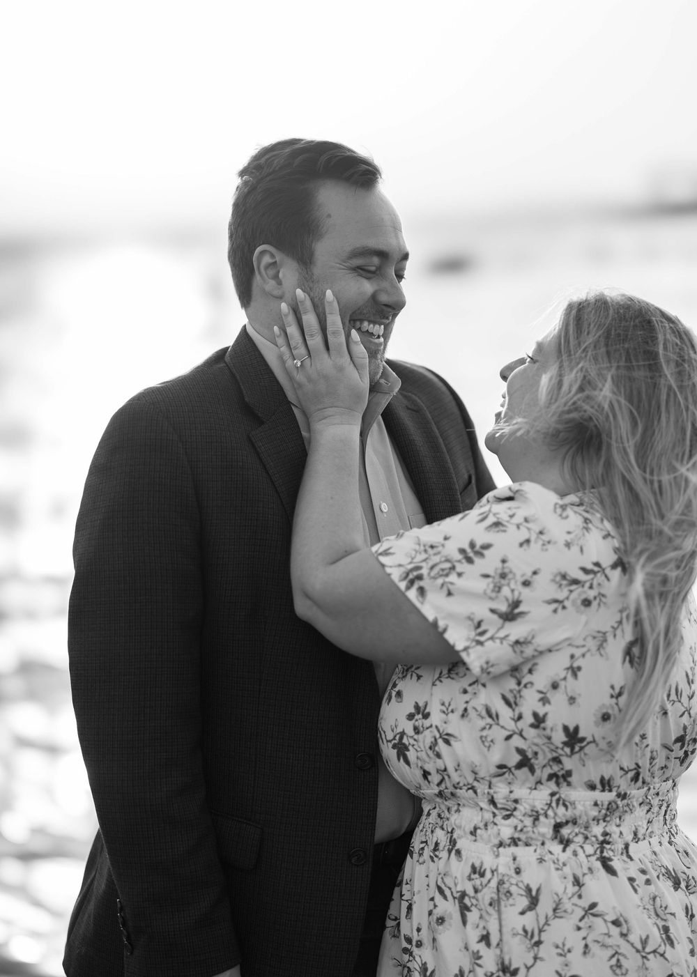 A romantic black and white photo of a couple laughing together by the water in an intimate moment.