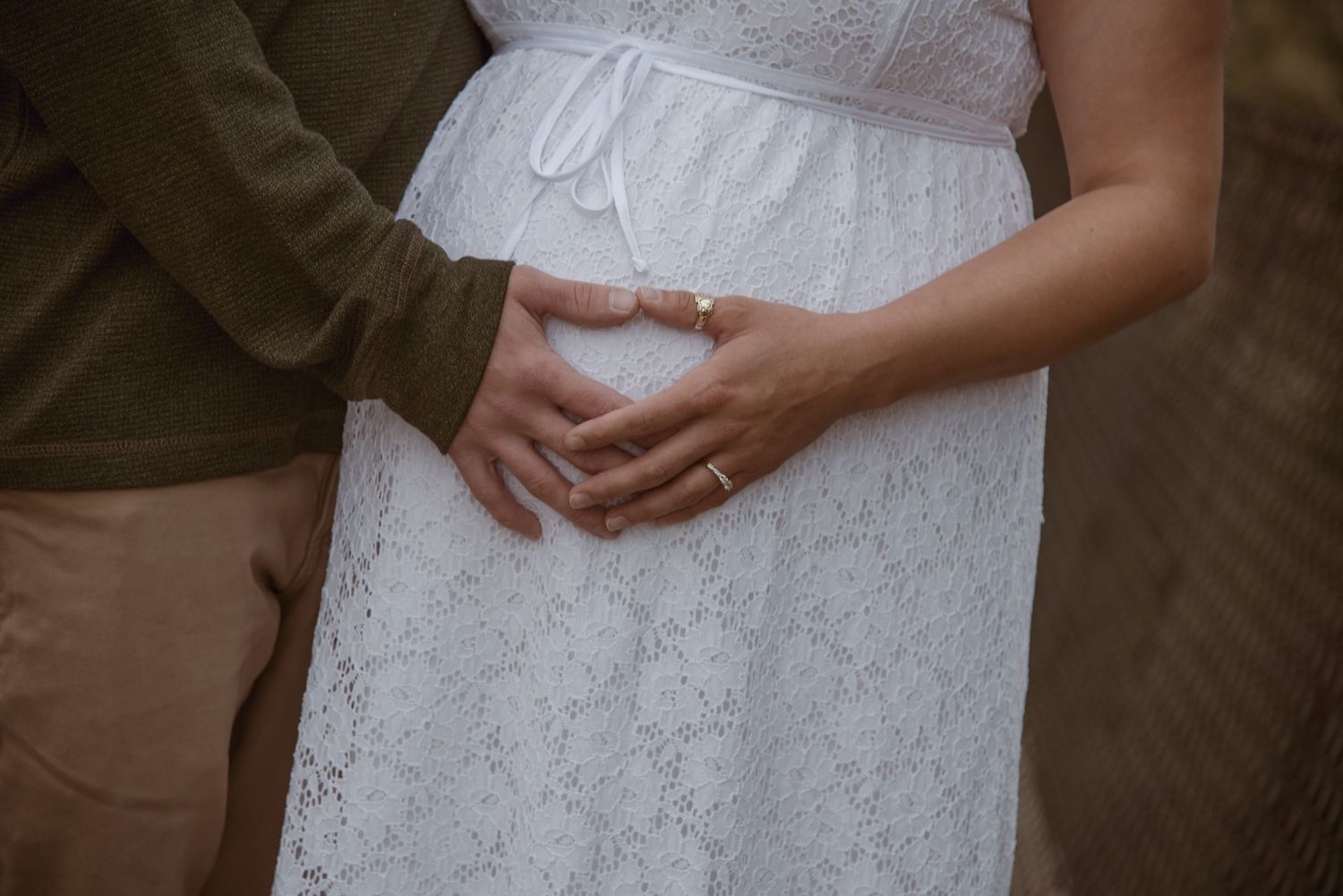 "Couple's hands forming a heart shape over a pregnant belly in a white lace dress. Whidbey Island maternity photography session.