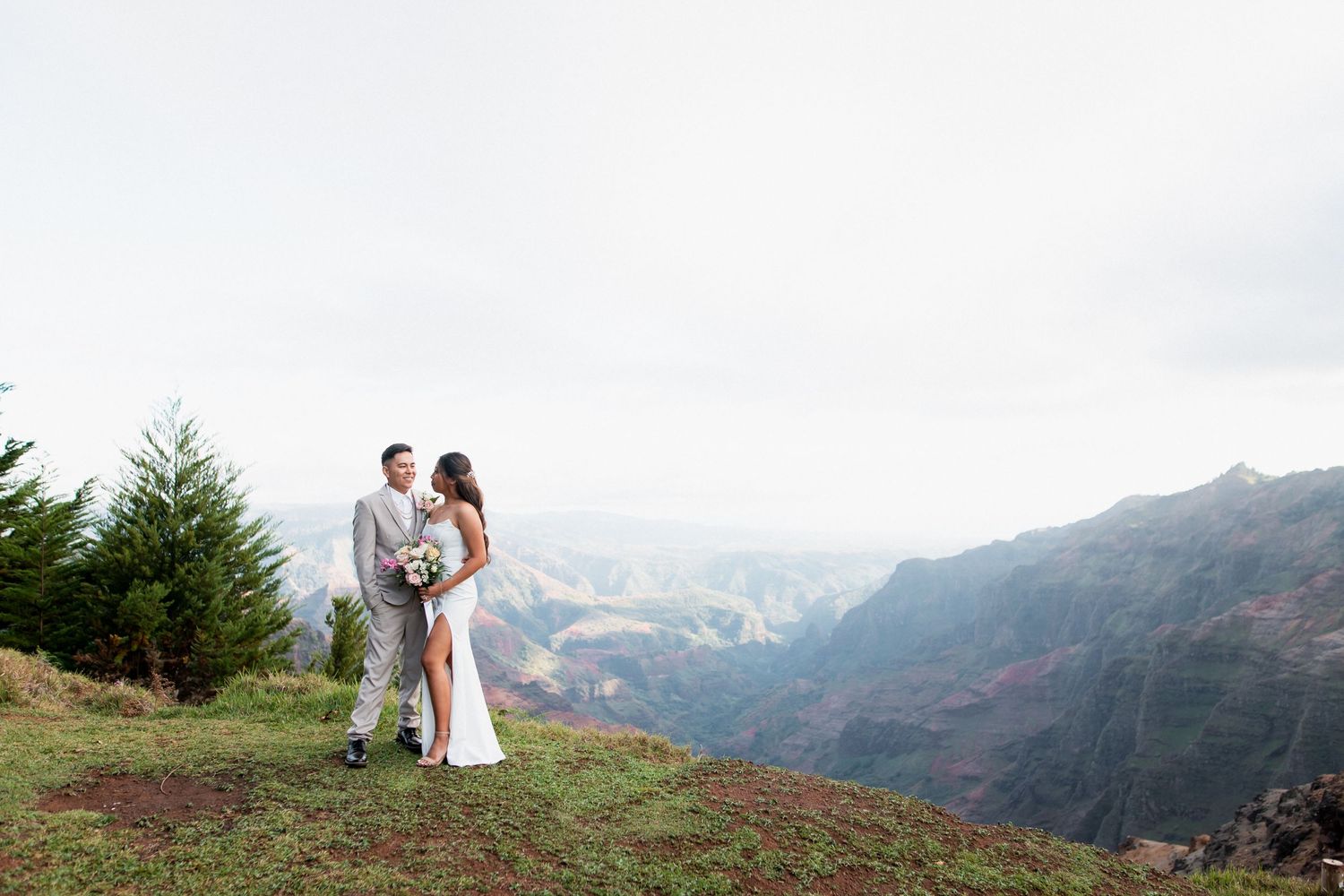 Bride and groom gazing into each other's eyes near the edge of a cliff in Kauai, Hawaii, with stunning canyon views in the background.