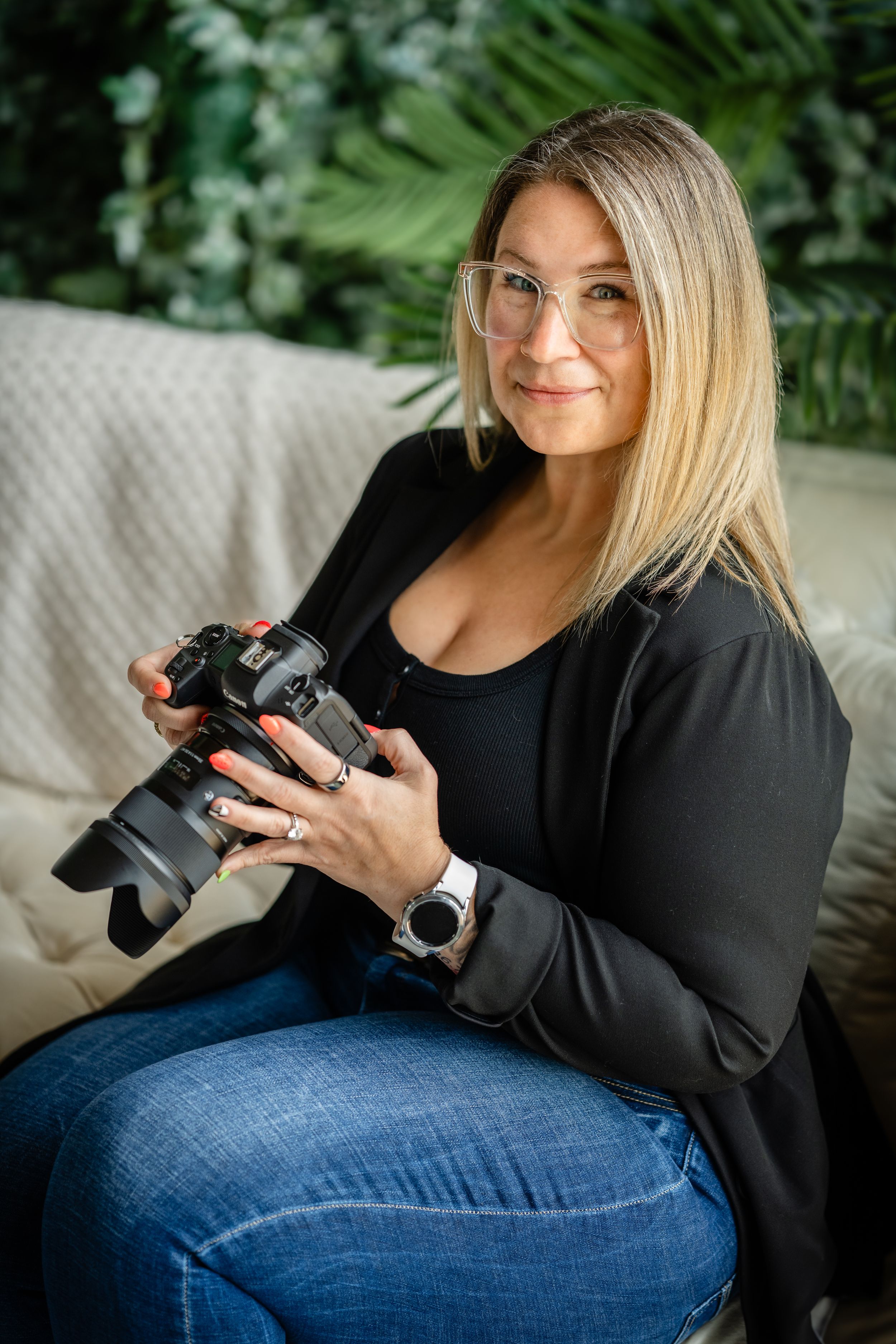 Professional photographer wearing black blazer and jeans examines digital camera while sitting comfortably on chair.