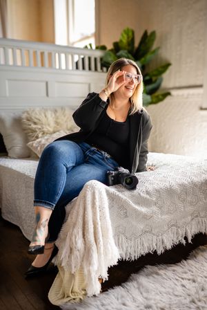 A casual photographer relaxes on a white lace-covered couch with a camera, wearing jeans and a black sweater.