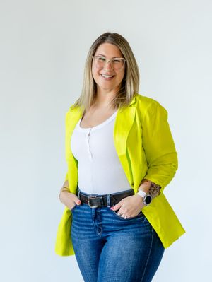 Professional wearing a bright yellow blazer with white top and jeans stands confidently against white background.