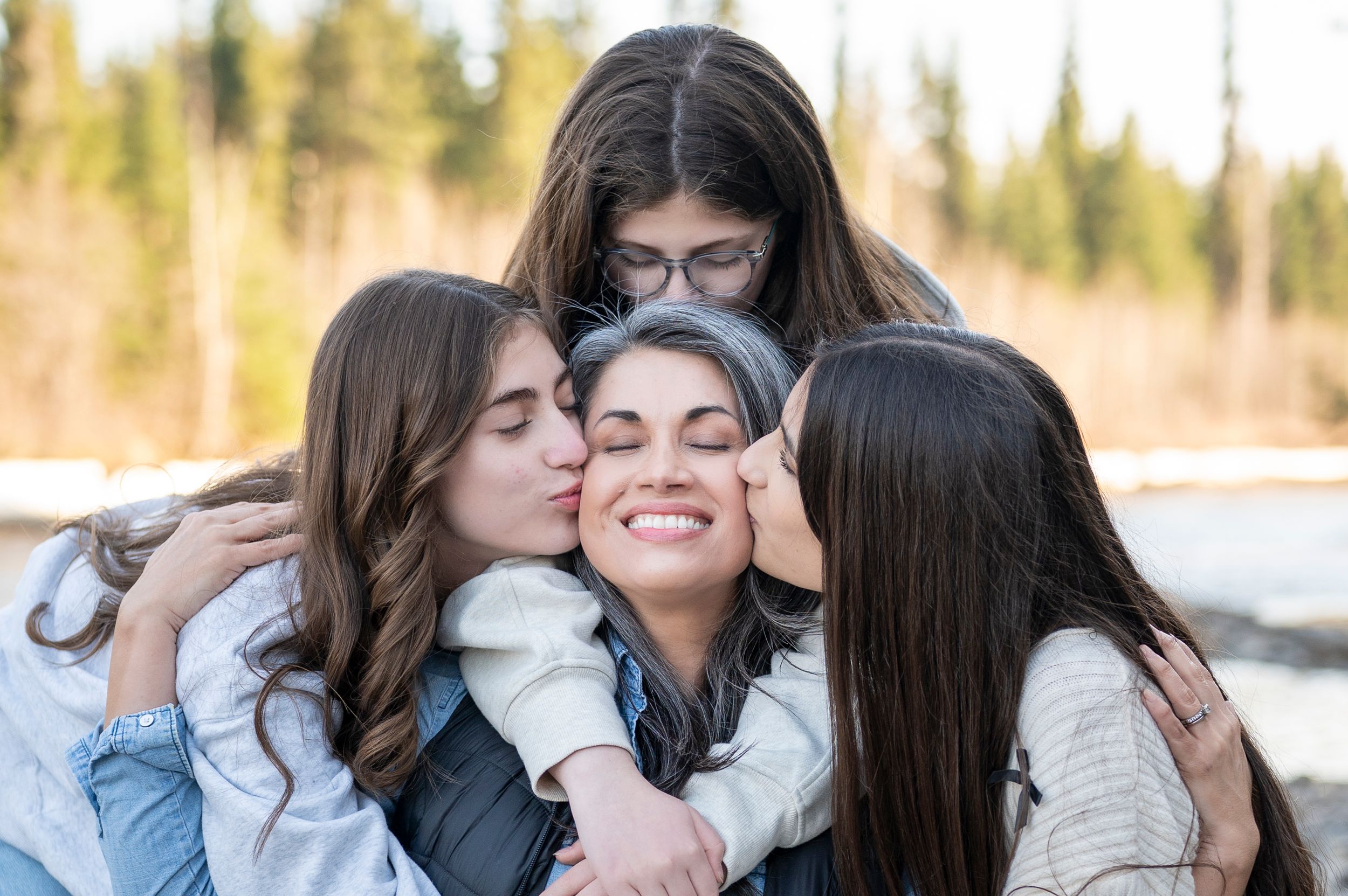 Four friends share a joyful group hug while spending time together outdoors on a sunny day.