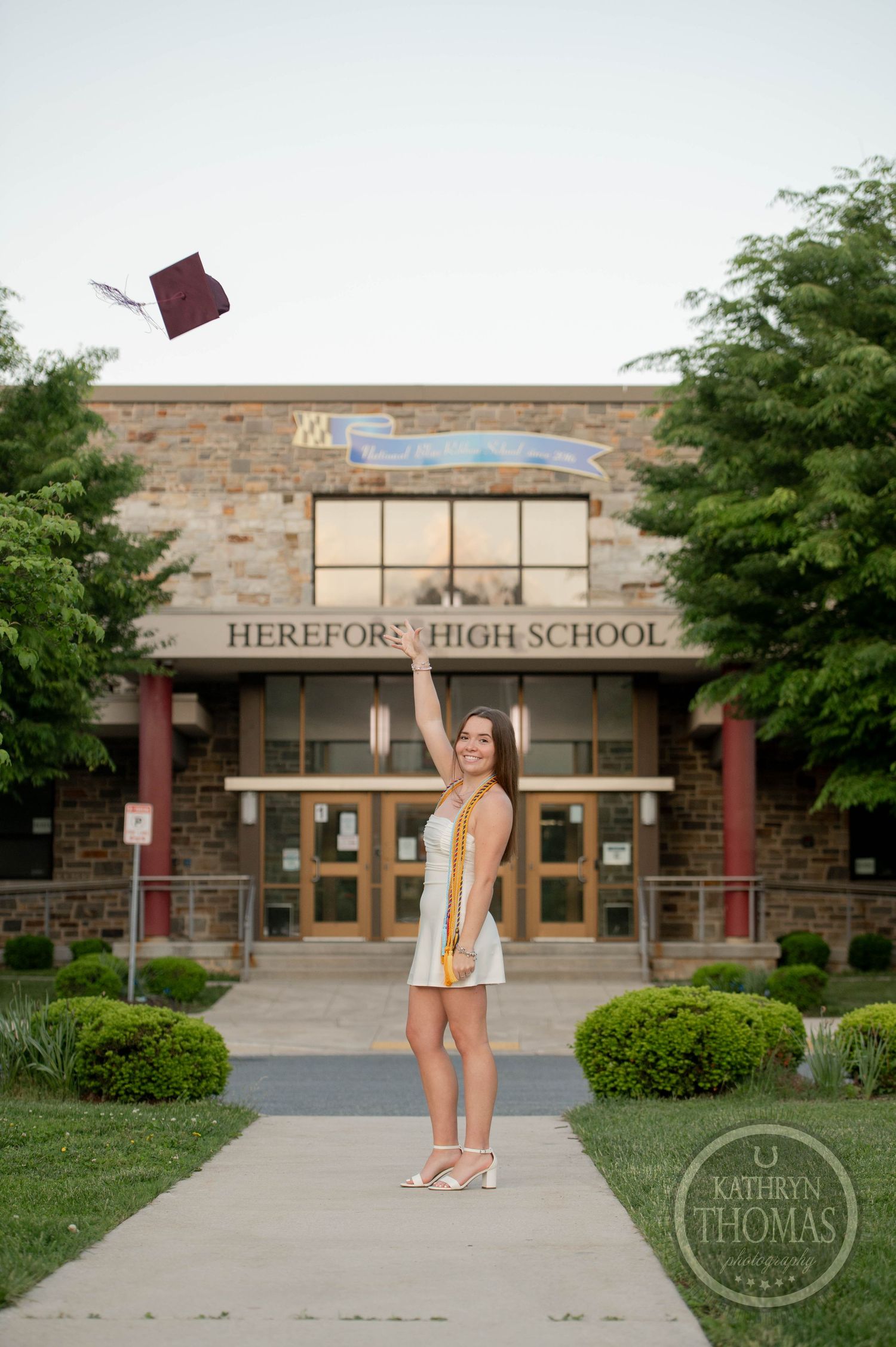 Graduate tosses mortarboard in celebration outside Hereford High School entrance on graduation day.
